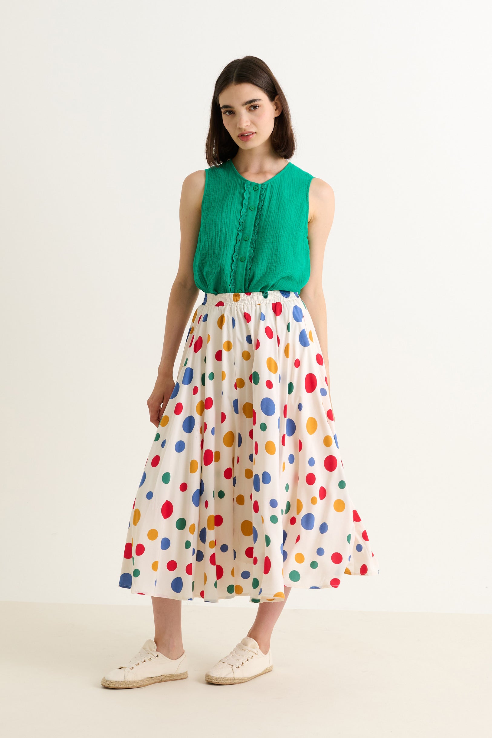 Woman wearing a green top and colorful polka dot skirt on a white background