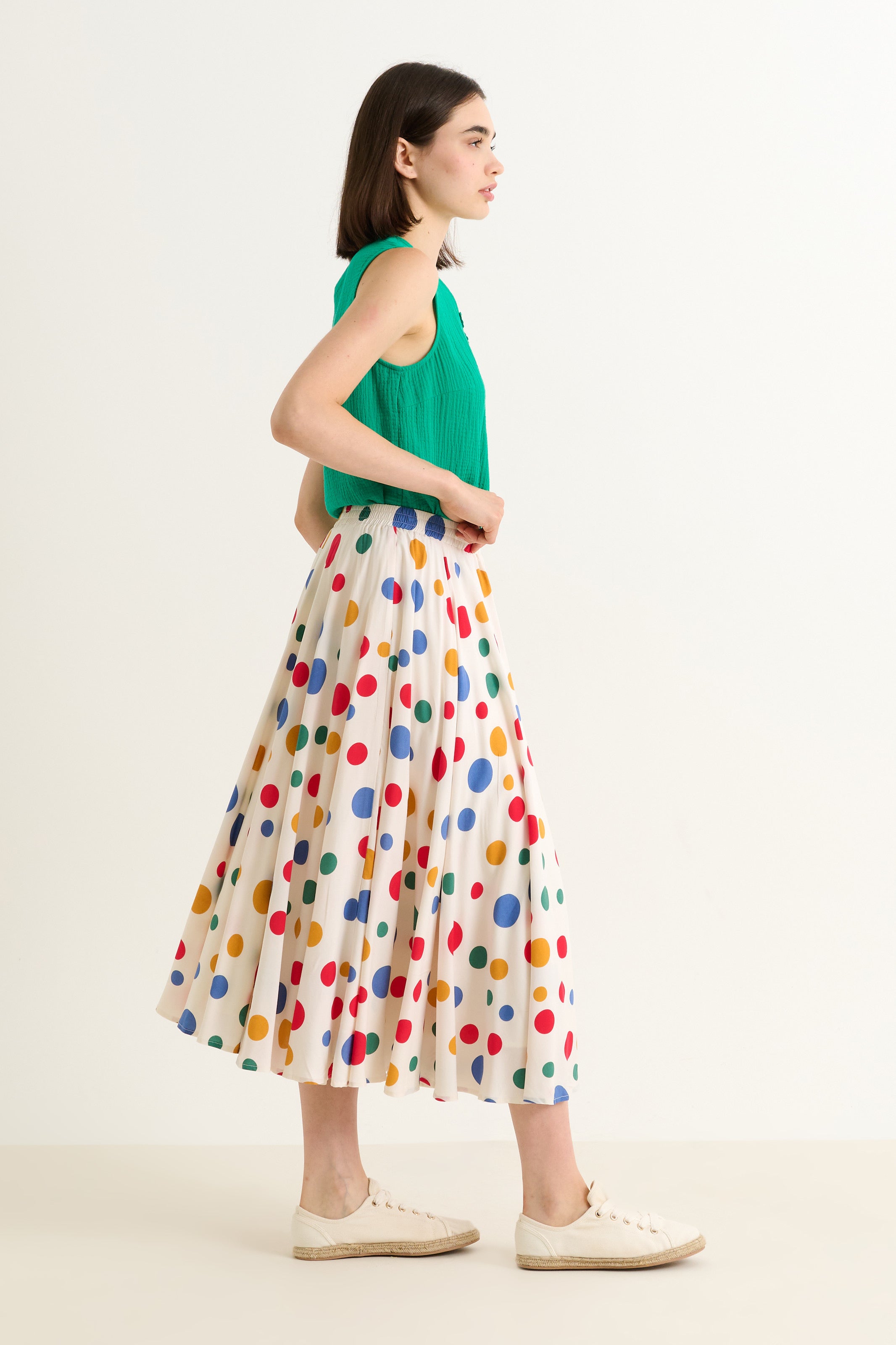 Woman wearing a green top and colorful polka dot skirt on a white background