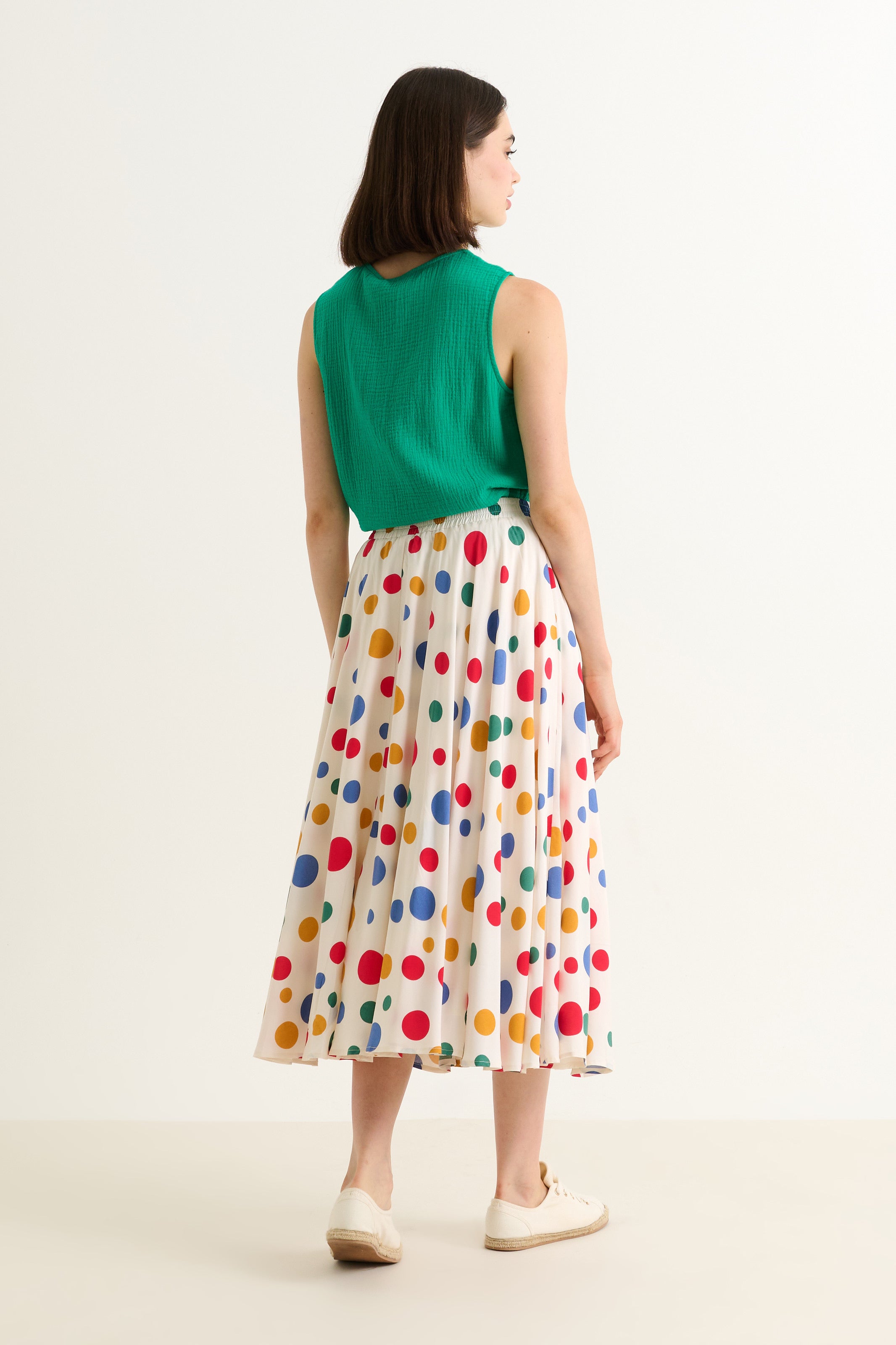 Woman wearing a green top and colorful polka dot skirt on a white background