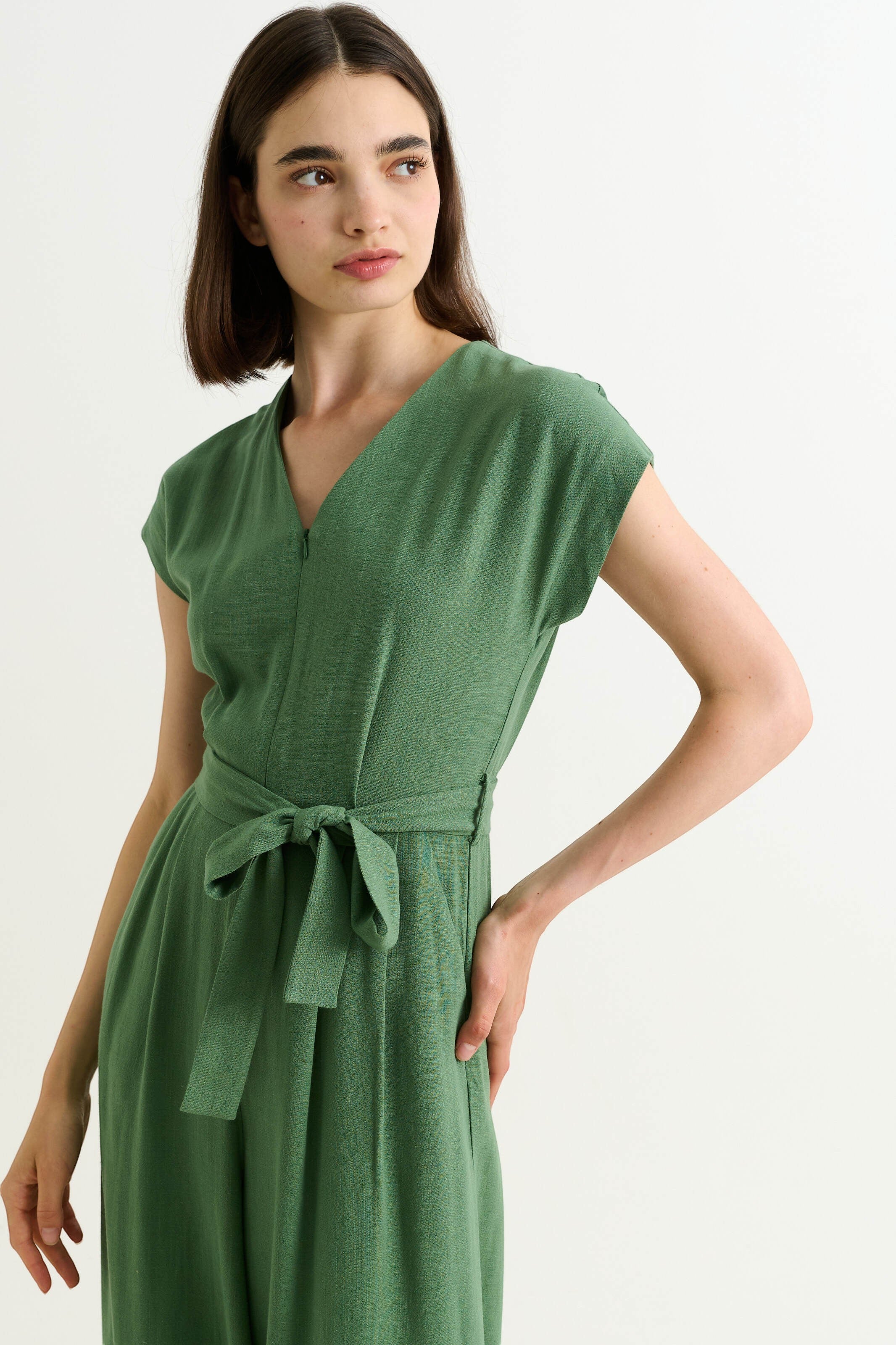 green linen mix wide-leg jumpsuit with V-neck, extended shoulders, self belt, and zip front.