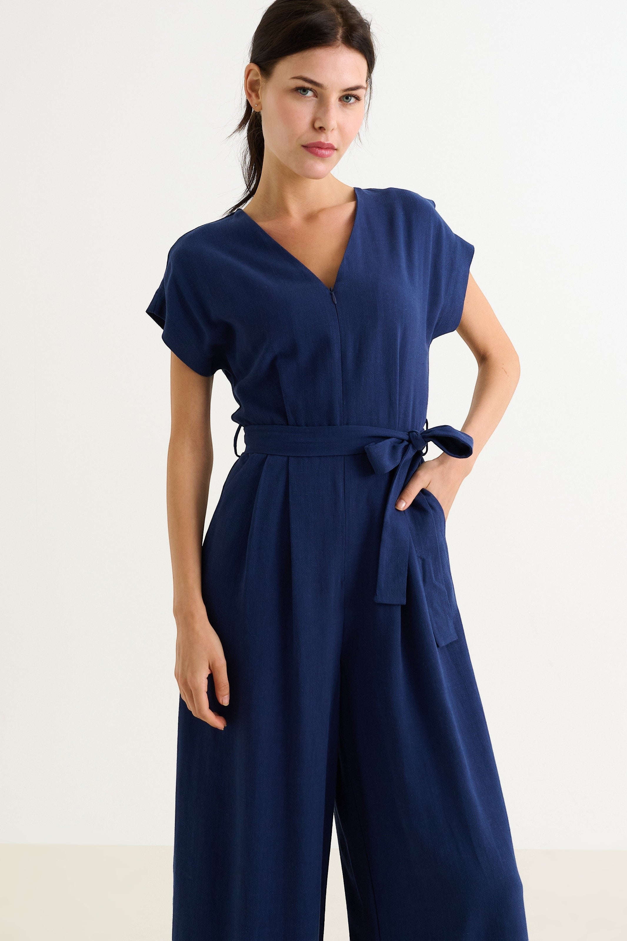 navy linen mix wide-leg jumpsuit with V-neck, extended shoulders, zip front, elasticated waist, self belt, and pockets.