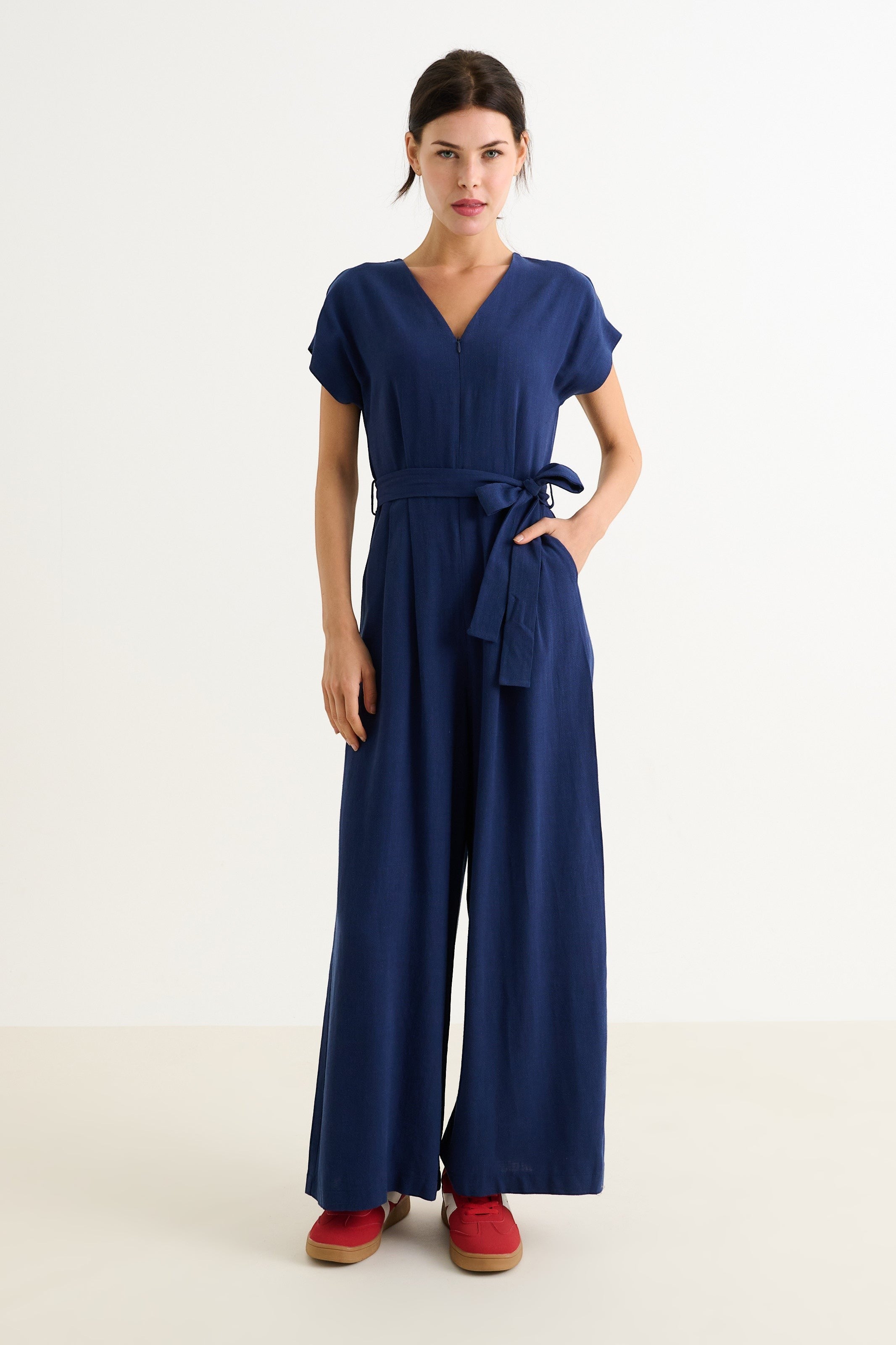 navy linen mix wide-leg jumpsuit with V-neck, extended shoulders, zip front, elasticated waist, self belt, and pockets.