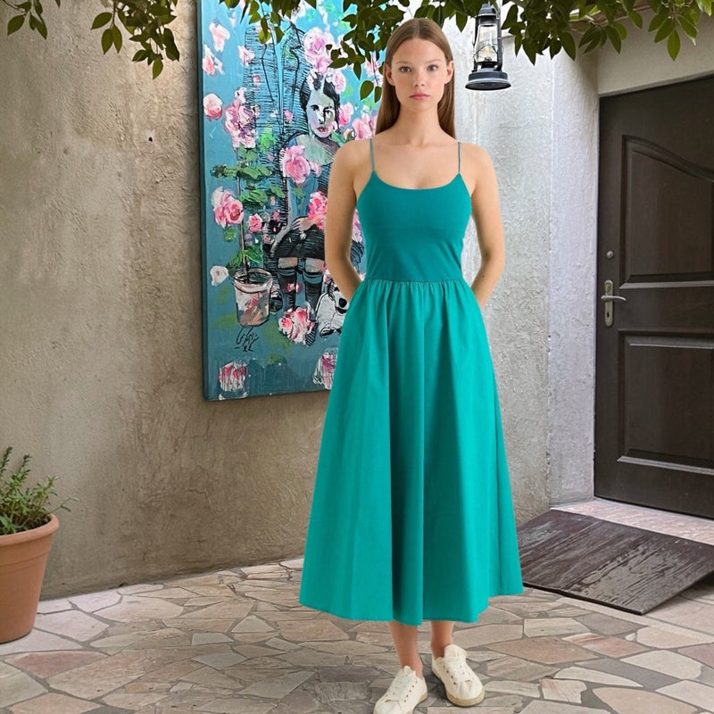 Model wears the Soumia recycled cotton midaxi dress in sea green, standing in a courtyard beside a floral painting