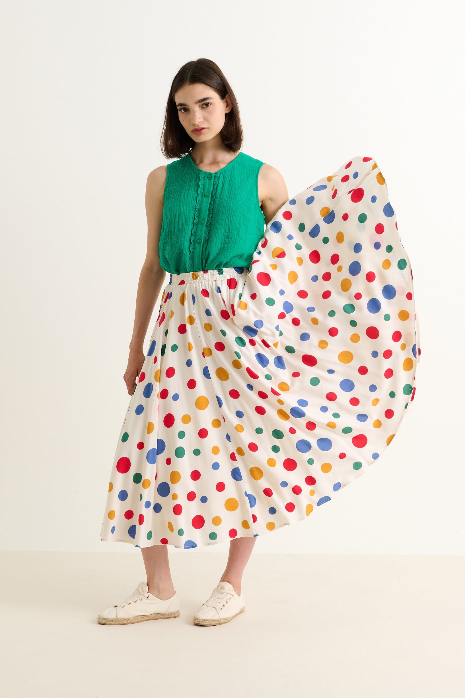 Woman wearing a green top and colorful polka dot skirt on a white background