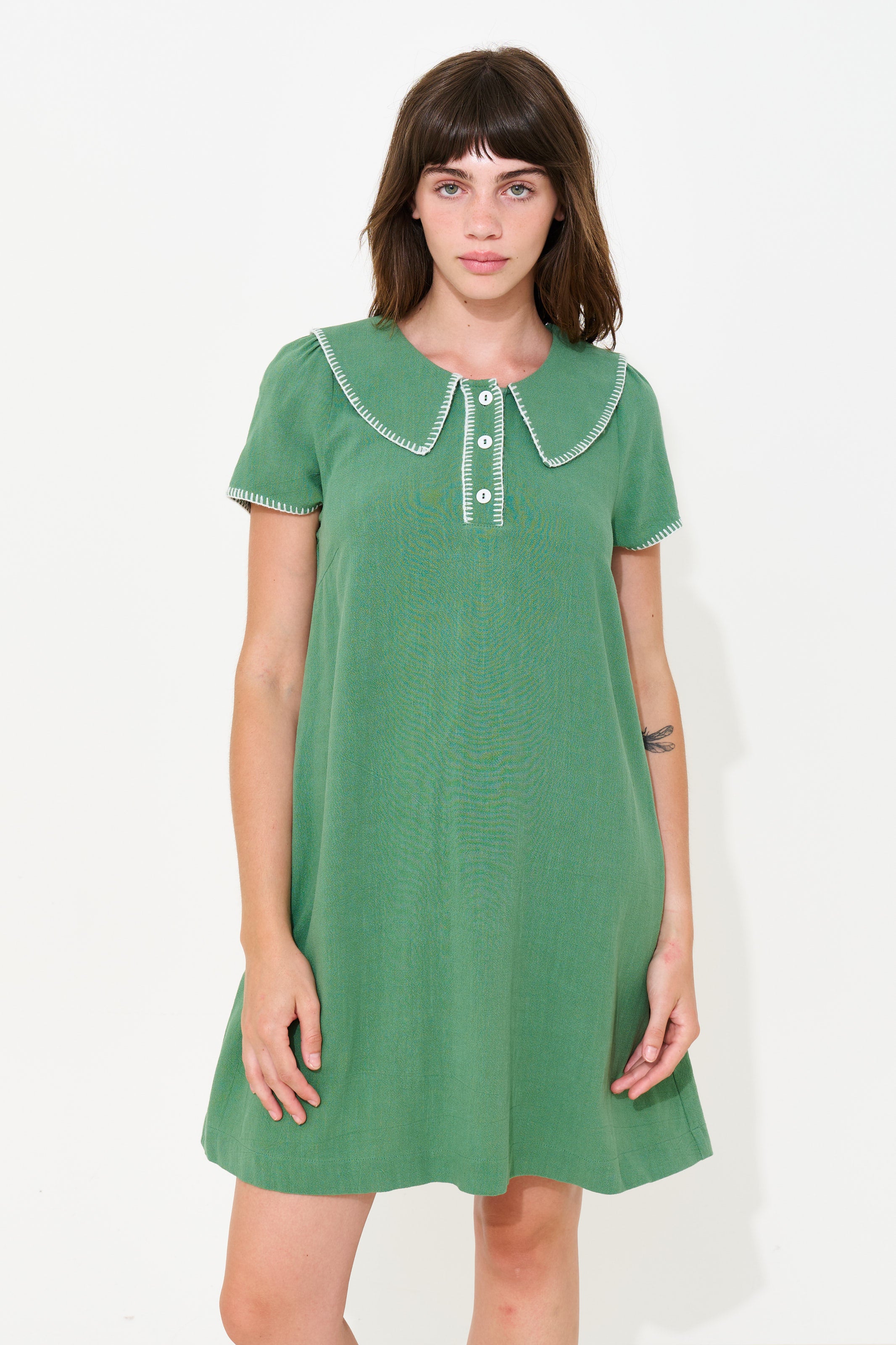 A woman modeling a green short-sleeve dress with a large Peter Pan collar and white trim details, set against a plain white studio background.
