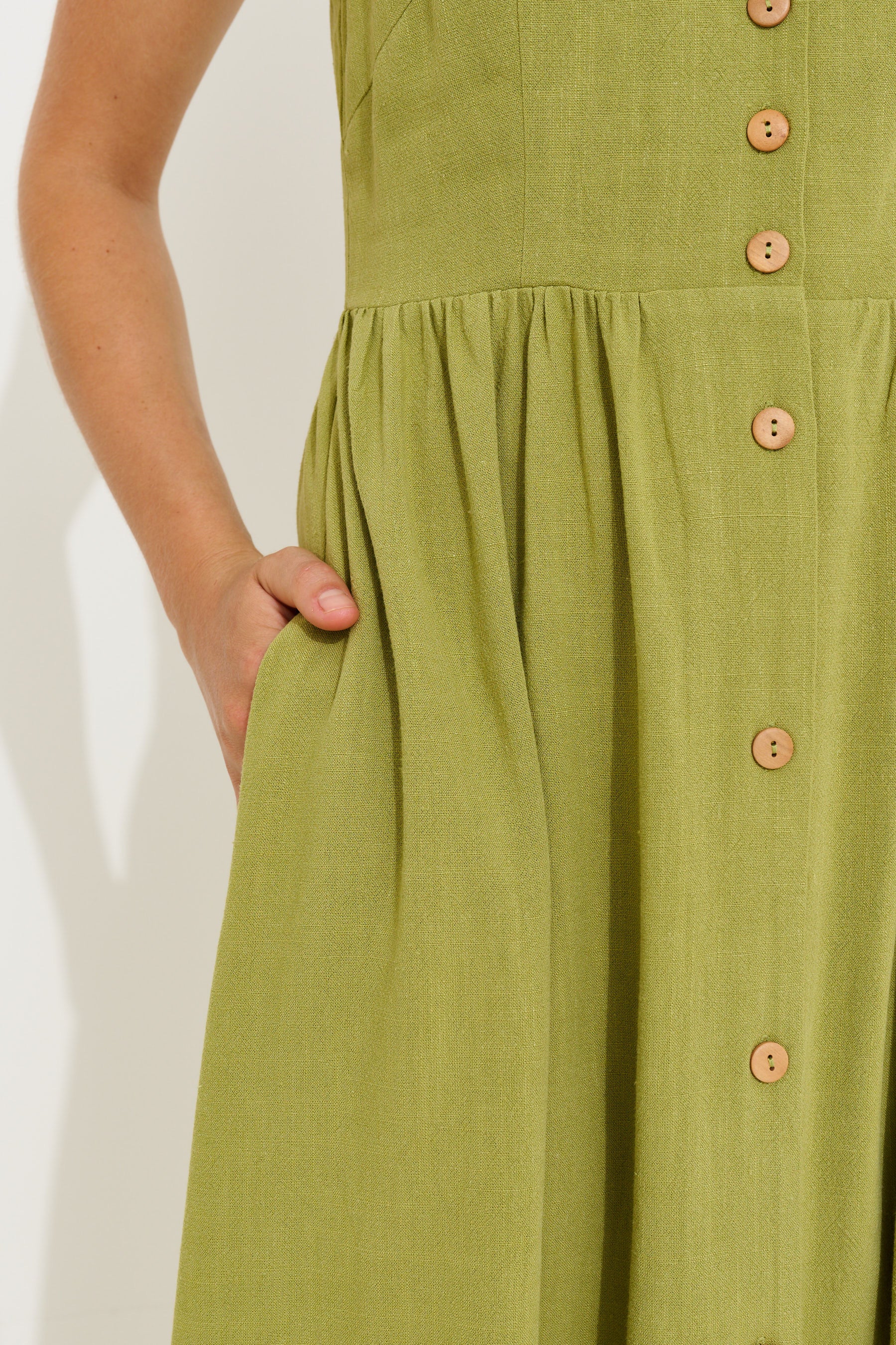 Close-up of a light olive green linen dress with a button-down front and side pockets, worn by a model.