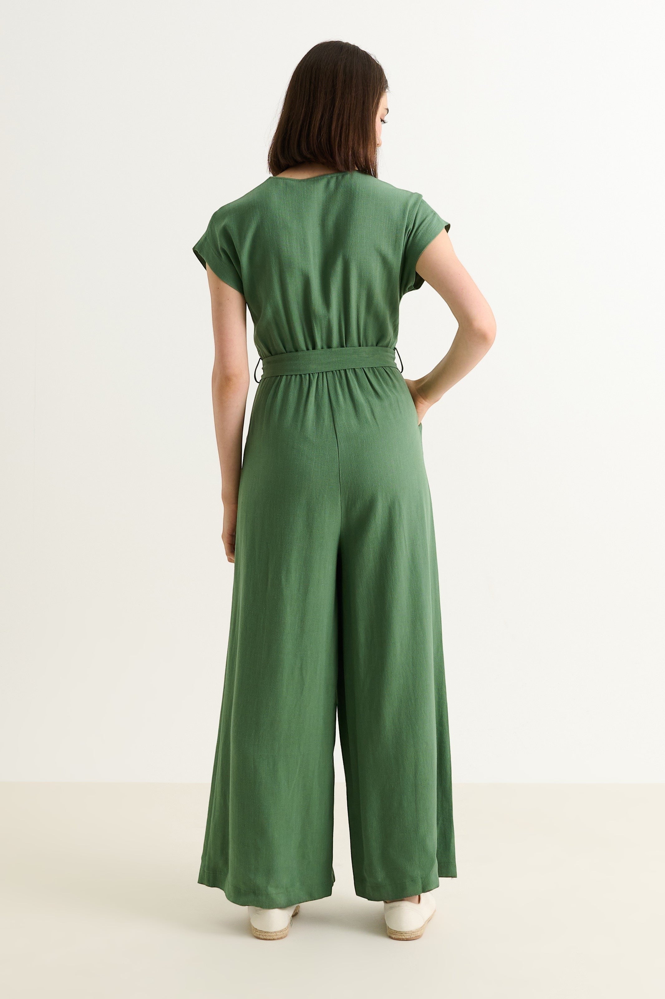 green linen mix wide-leg jumpsuit with V-neck, extended shoulders, self belt, and zip front.