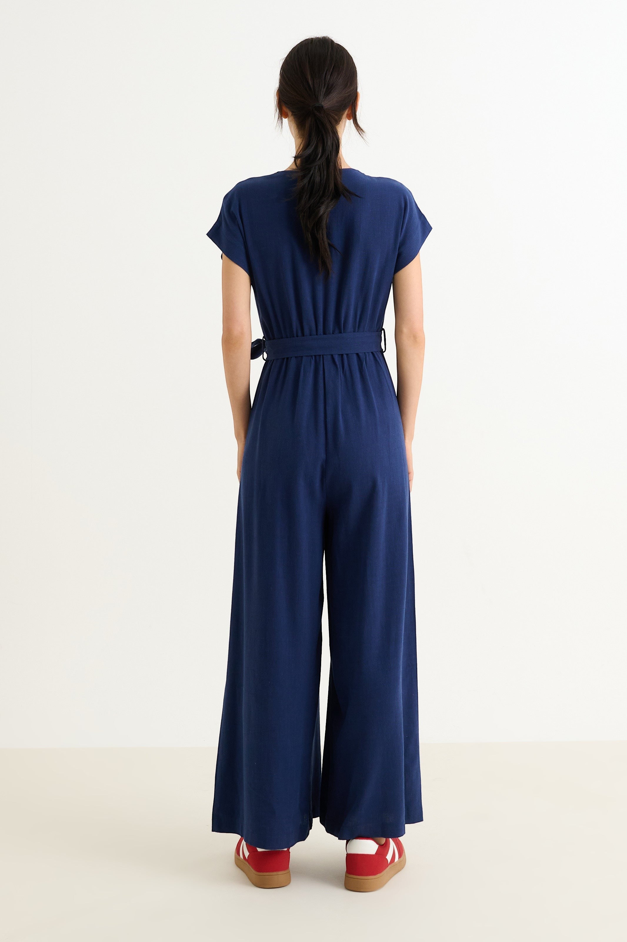 navy linen mix wide-leg jumpsuit with V-neck, extended shoulders, zip front, elasticated waist, self belt, and pockets.