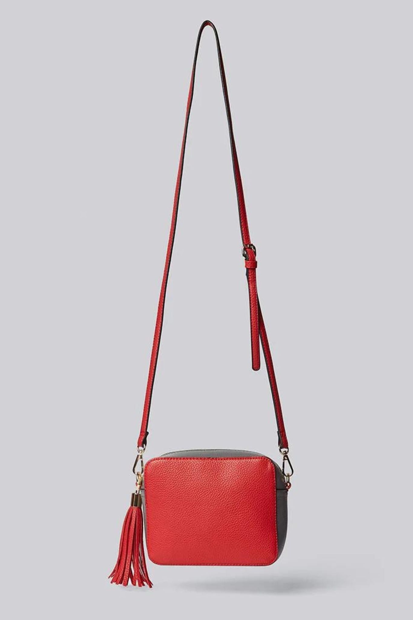 Louche Daisy red and grey panelled crossbody camera bag with black piping, gold hardware and red leather tassel pull, hung by long red shoulder strap on a grey background.